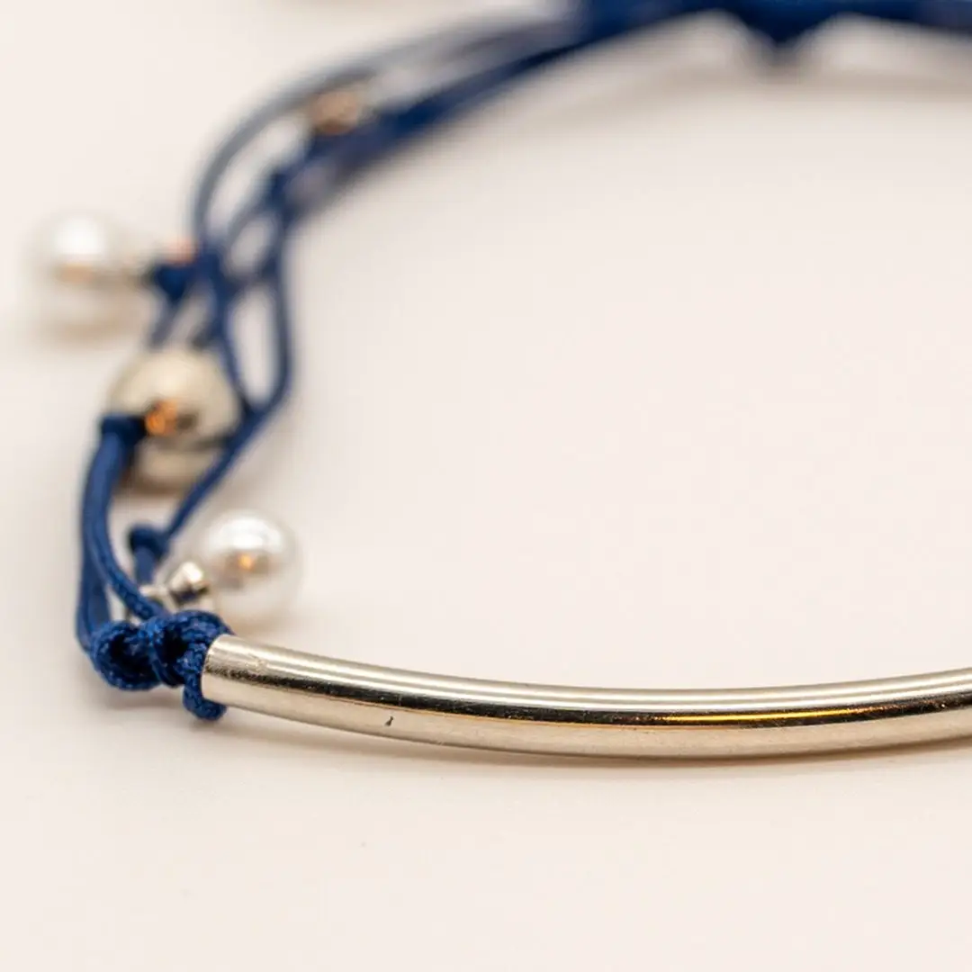Pormenor da Pulseira Âncora — Cordão azul-marinho ajustável (macramé) com tubo central curvo e contas em aço prateado