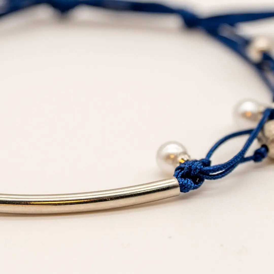 Pormenor da Pulseira Âncora — Cordão azul-marinho ajustável (macramé) com tubo central curvo e contas em aço prateado