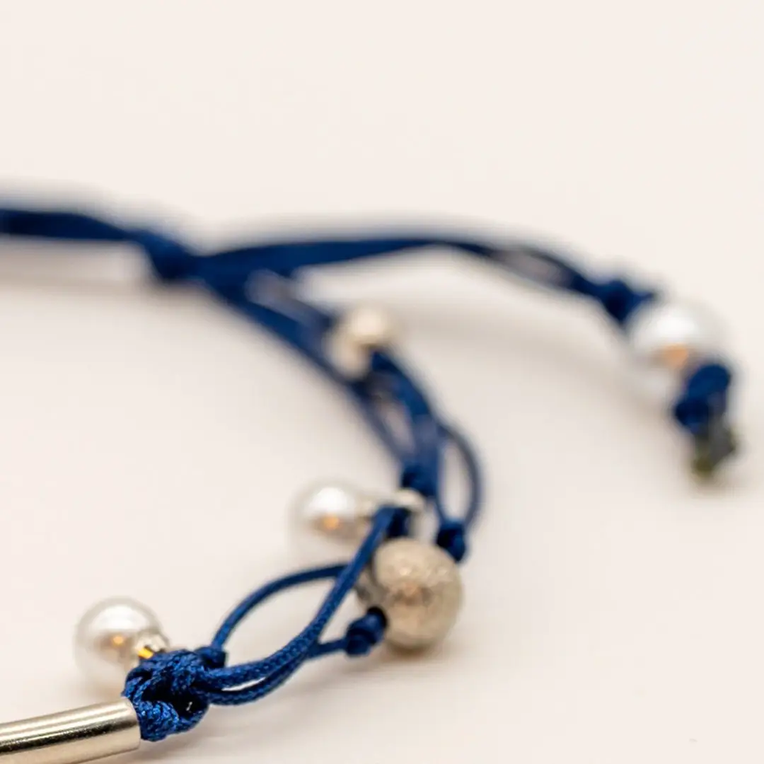 Pormenor da Pulseira Âncora — Cordão azul-marinho ajustável (macramé) com tubo central curvo e contas em aço prateado