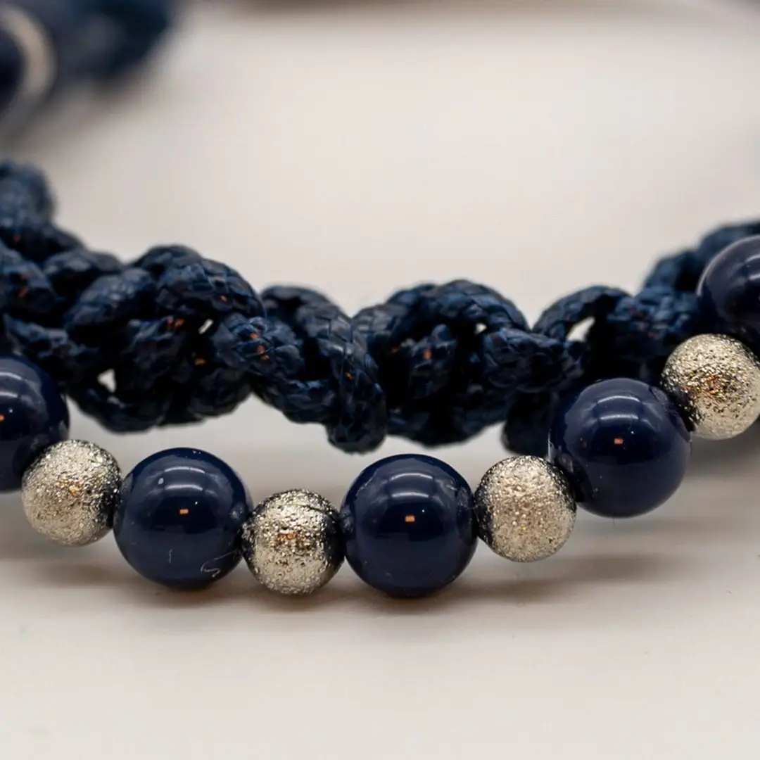Pormenor da Pulseira Nó do Mar — Pulseira dupla de cordão azul-marinho trançado (macramé) com contas azul-marinho e prateadas texturadas e fecho magnético em aço