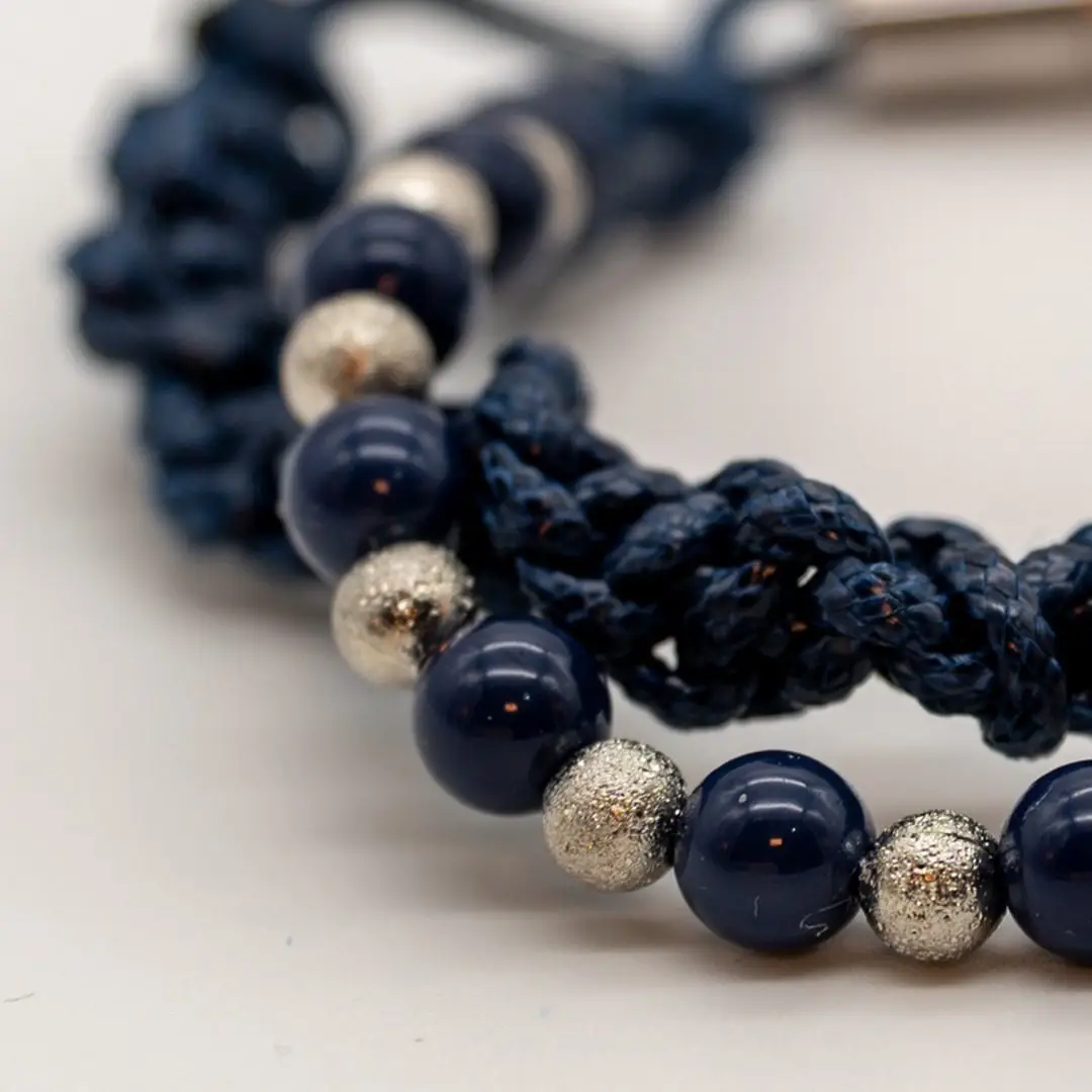 Pormenor da Pulseira Nó do Mar — Pulseira dupla de cordão azul-marinho trançado (macramé) com contas azul-marinho e prateadas texturadas e fecho magnético em aço