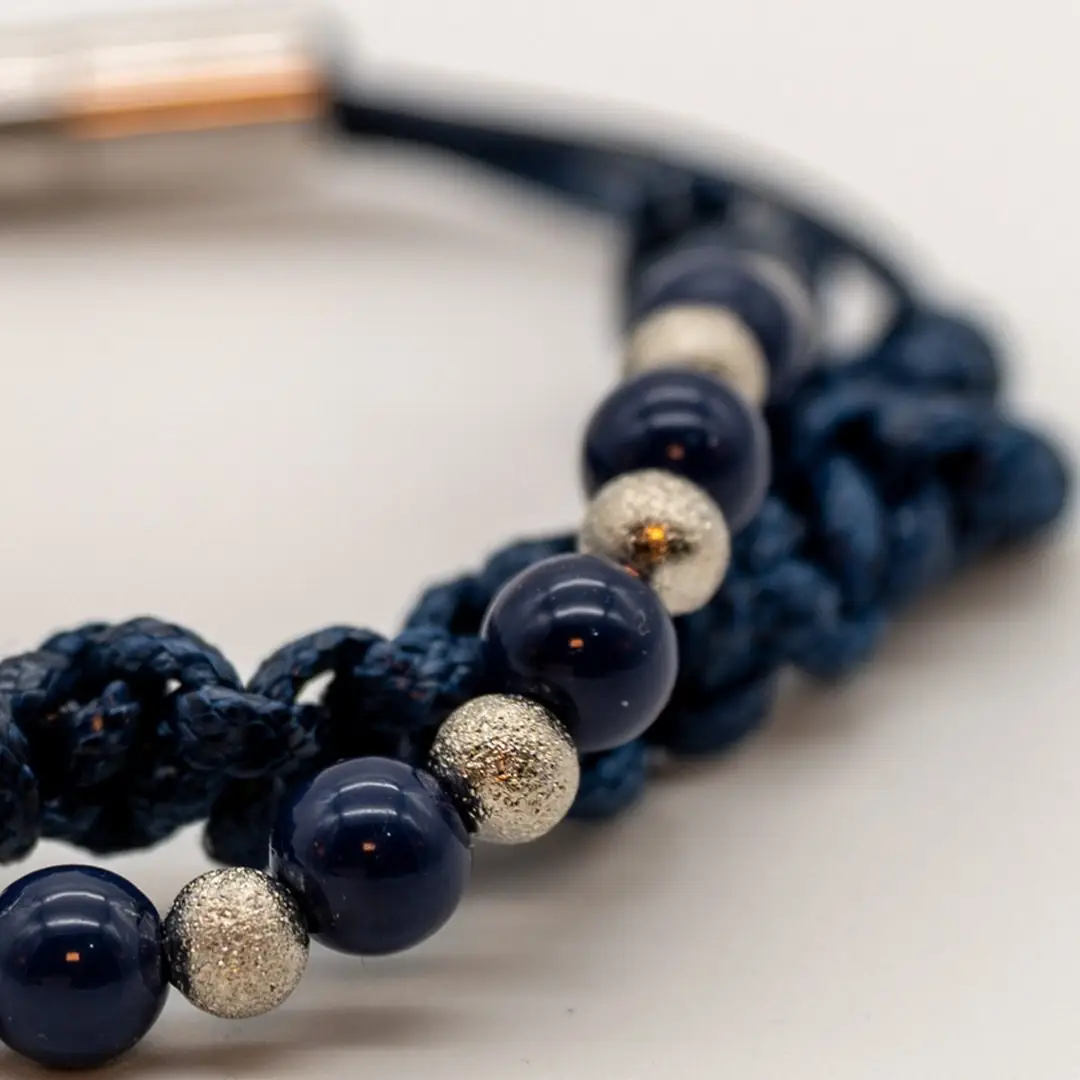 Pormenor da Pulseira Nó do Mar — Pulseira dupla de cordão azul-marinho trançado (macramé) com contas azul-marinho e prateadas texturadas e fecho magnético em aço
