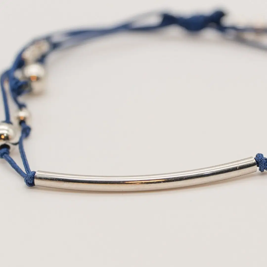 Pormenor da Pulseira Rumo — Cordão azul-marinho ajustável (macramé) com tubo central curvo e contas em aço prateado