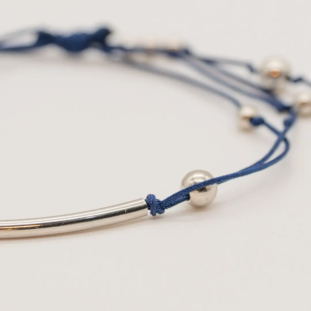 Pormenor da Pulseira Rumo — Cordão azul-marinho ajustável (macramé) com tubo central curvo e contas em aço prateado