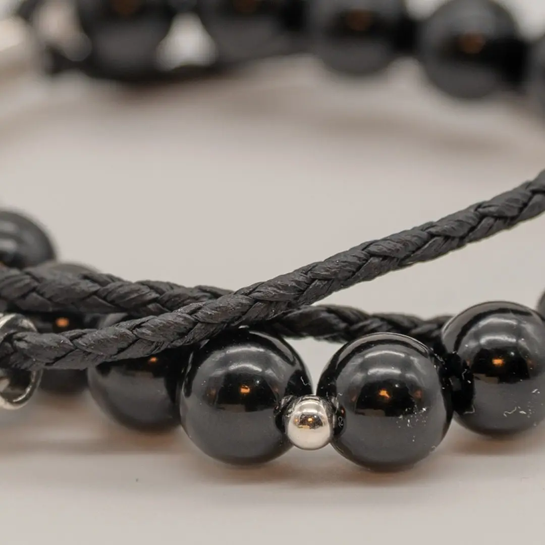 Pormenor da Pulseira Timoneiro — Pulseira dupla — fio de contas hematite + cordão preto trançado com tubo central gravado em aço