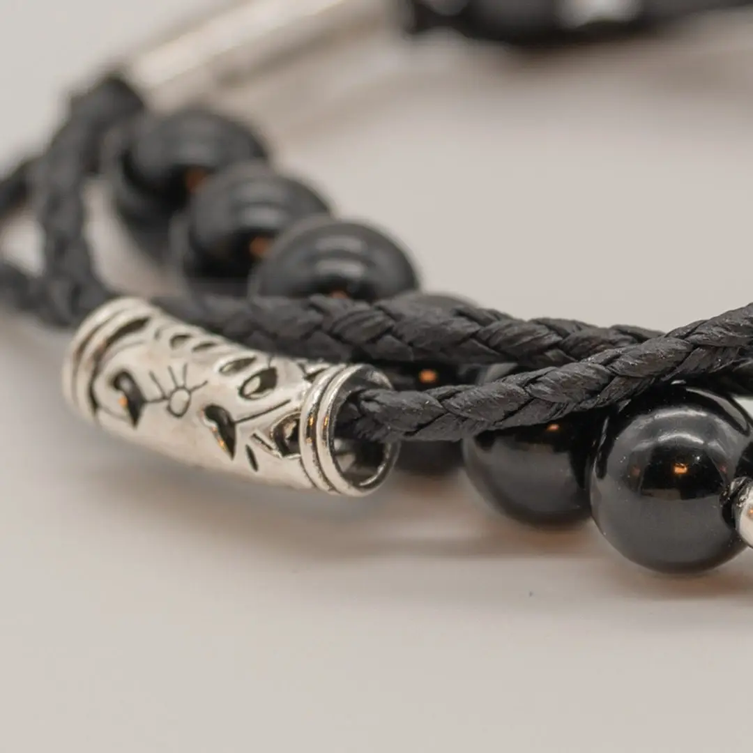 Pormenor da Pulseira Timoneiro — Pulseira dupla — fio de contas hematite + cordão preto trançado com tubo central gravado em aço