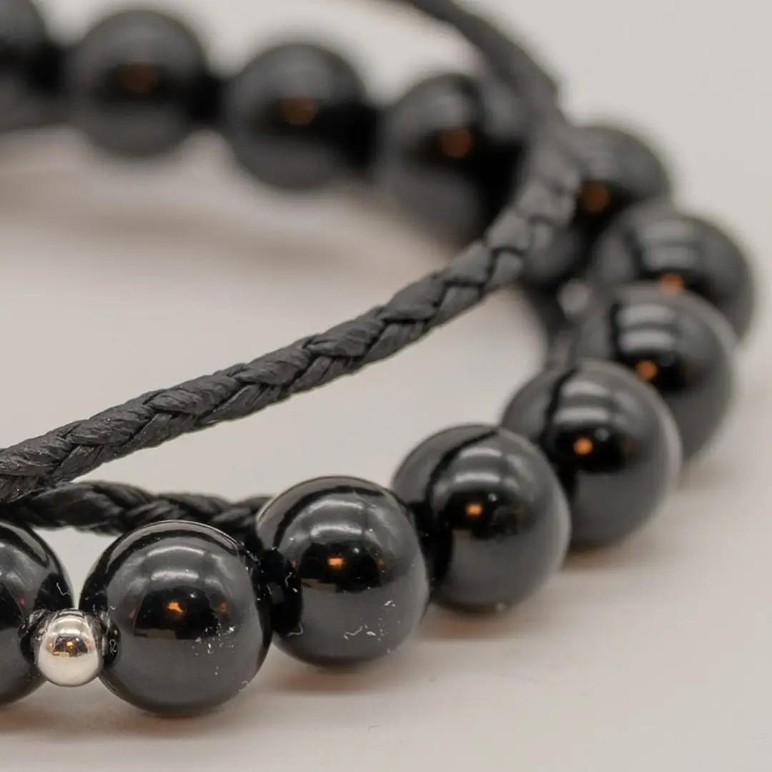 Pormenor da Pulseira Timoneiro — Pulseira dupla — fio de contas hematite + cordão preto trançado com tubo central gravado em aço